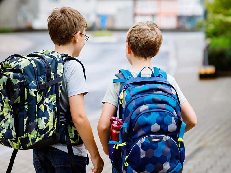 Two little kid boys with backpack or satchel. Schoolkids on the way to school. Healthy adorable children, brothers and best friends outdoors on the street leaving home. Back to school. Happy siblings.