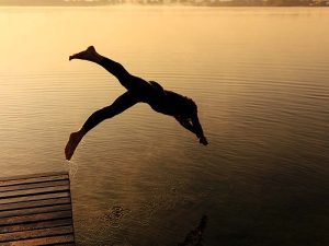 Silhouette of active sportsman dashing into foggy lake