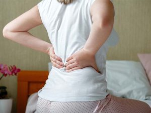 Back pain woman getting after wake up. Sick person with Backache in spine. Unrecognizable woman in bedroom have lumbar, lower back pain after sleeping.
